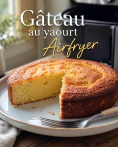 Gros plan d'un gâteau au yaourt parfaitement cuit dans un Airfryer, croûte dorée, une part coupée montrant une mie humide, sur une assiette en céramique avec une fourchette, lumière du jour naturelle et douce, panier de l'Airfryer flou en arrière-plan, cuisine chaleureuse, tons chauds, avec texte superposé 'Gâteau au yaourt Airfryer'.